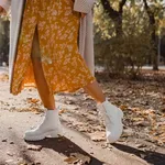 close-up legs in stylish white boots footwear of young woman in yellow printed dress