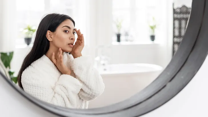 Young asian woman looking at mirror, checking skin