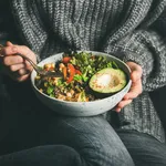 Woman in sweater eating fresh salad, avocado, beans and vegetables