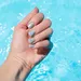 Hand met blauwe nagellak op nagels boven zwembad