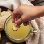 Cup of ginger tea on wooden background and woman hand