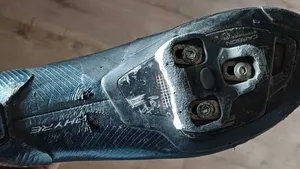 Close-up van de zool van een wielrenschoen met een duidelijk versleten schoenplaatje en beschadigde zool, als voorbeeld van cleats die aandacht en afstelling nodig hebben.
