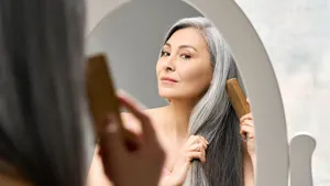 Mature mid aged senior Asian woman looking at mirror combing her gray hair.