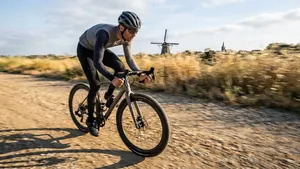 Mannelijke wielrenner met helm op gravelbike rijdt snel over een zonnig gravelpad, met de nieuwe Continental Terra Competition band zichtbaar op de voorgrond.