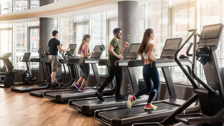 Group of four people running on treadmills in fitness gym