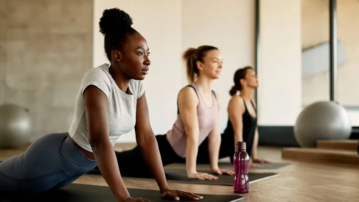 Black female athlete doing stretching exercises while warming up with group of women at health club.