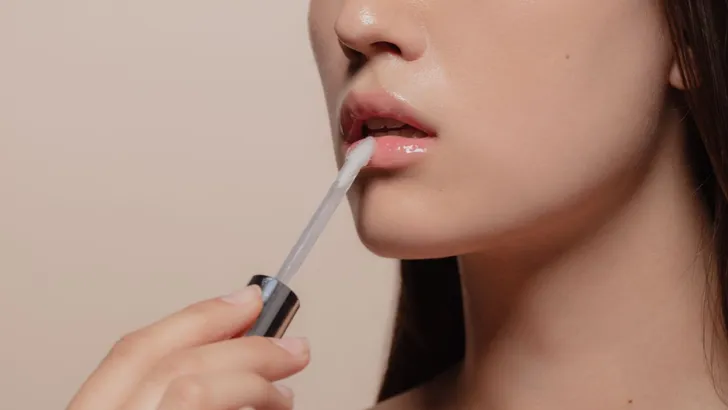 Vrouw brengt glanzende lipgloss aan voor een glossy look.