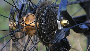 Gedetailleerde close-up van een fietscassette en ketting, met scherpe focus op de tandwielen. De dramatische belichting op een donkere achtergrond accentueert de metalen onderdelen van de aandrijflijn