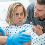 In the Hospital Woman in Labor Pushes to Give Birth, Obstetricians Assisting, Husband Holds Her Hand for Support. Modern Delivery Ward with Professional Midwives.