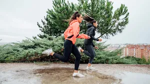 Two beautiful women running in park with rain and puddles.