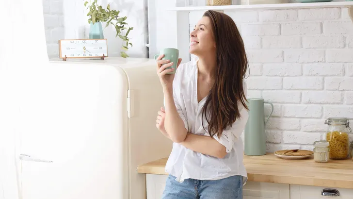 Young happy woman drinking coffee on the kitchen in the morning