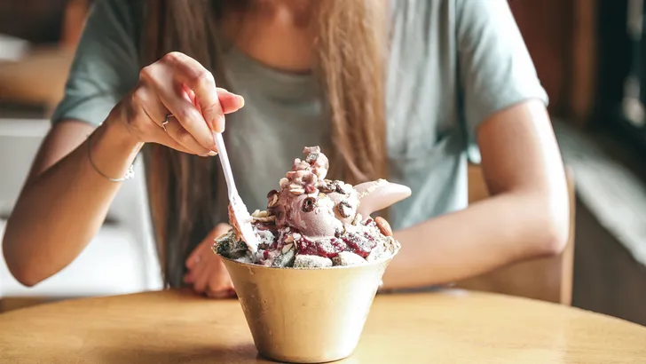Female young lady eat Korean Bingsu ice with chocolate icecream. with ricecake and nuts. selective focus on bingsu blur people.