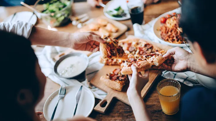 Close up of a young group of friends passing and serving food while enjoying together. They are having fun, chatting and feasting on food and drinks at dinner party