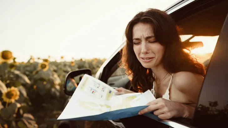 Lost young woman sitting in her car in the countryside and looking at map