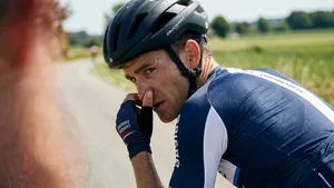 Een mannelijke wielrenner in professionele outfit draait tijdens het fietsen zijn hoofd opzij, een voorbeeld van snotiquette in de praktijk.