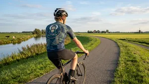 Mannelijke wielrenner met helm fietst ontspannen en lachend op een racefiets door een zonnig landschap.