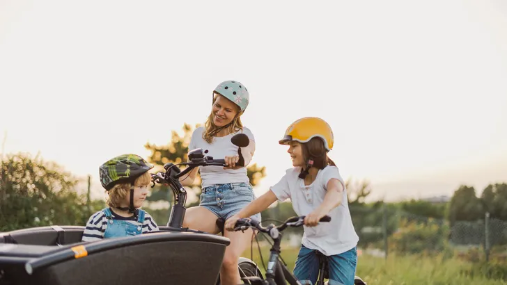 Vrouw met kinderen bij een elektrische bakfiets in een landelijke omgeving
