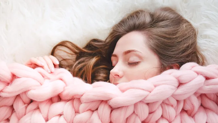 Young woman with long brown hair sleeping under warm knitted peach color throw blanket