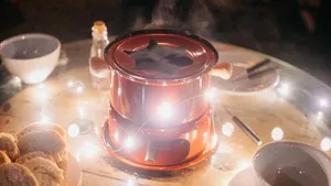 Sfeervol gedekte kersttafel met een stijlvolle kaasfondueset, omringd door wijnglazen, brood en kaarsen voor een chic diner tijdens de feestdagen.