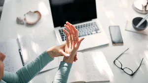 Woman with hand, joint, arm and finger pain, stretching and massaging during work on a laptop.