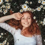 Beautiful young girl with curly red hair in chamomile field