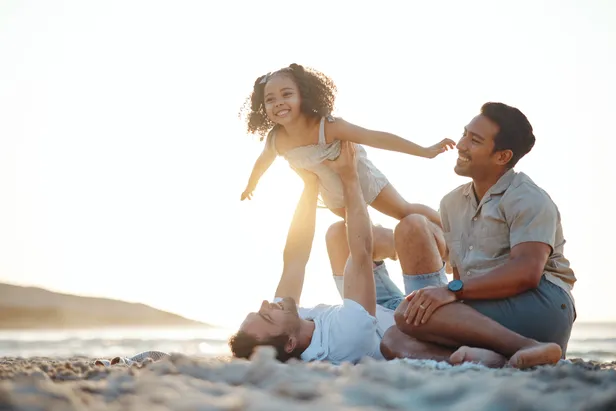 Onderzoek Booking.com LHTBI+ reizigers 2026: twee mannen die op het strand met hun dochter spelen.