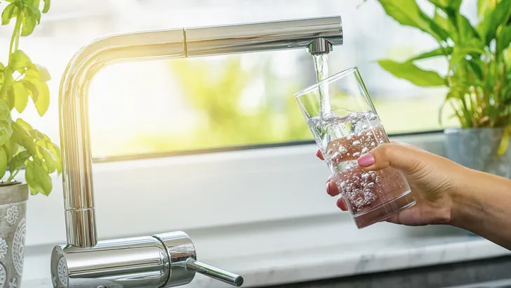 Hand houdt een glas water onder de waterkraan