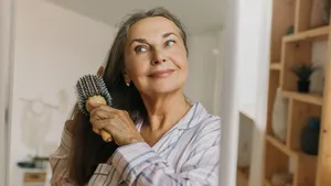 Zelfverzekerde vrouw van 40+ die met haar hand door haar volle haren gaat, als voorbeeld van goede verzorging bij haarverandering na je 40e