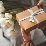 The child's hands hold a beautiful gift box with a ribbon and white tulips. Top view, close-up. Happy mother's day