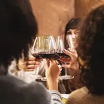 group of happy friends having a dinner and toasting red wine sitting at restaurant table