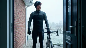 Mannelijke wielrenner in winterkleding met helm, klaar om te vertrekken op zijn geplande rustdag, kijkt zelfverzekerd naar buiten vanuit zijn deuropening.