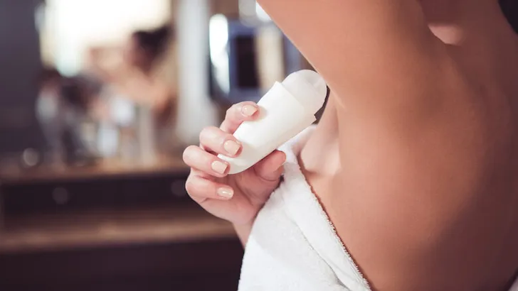 Woman in bath towel applying deodorant on armpit