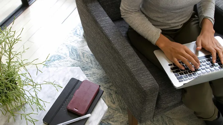 Administratieve baan – Foto van bovenaf genomen van persoon met laptop op schoot op fauteuil.