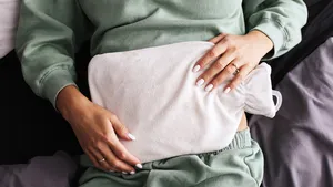 Warmwaterkruik op de buik, illustratie bij artikel over de houdbaarheidsdatum en veiligheid van warmwaterkruiken.