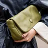 Vrouw in een lange zwarte leren jas houdt een groene handtas vast onder haar arm
