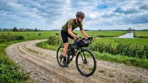Mannelijke wielrenner met helm op een gravelbike met een breed flare stuur, rijdend over een onverhard pad in de Nederlandse natuur.