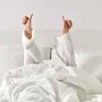 hands of woman lying in bed and showing thumbs up