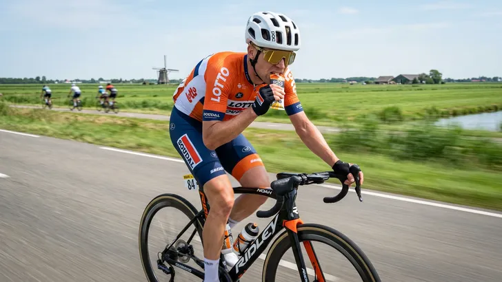 Actieportret van een mannelijke wielrenner die met zijn tanden een energiegel openbreekt tijdens een rit door de polder.