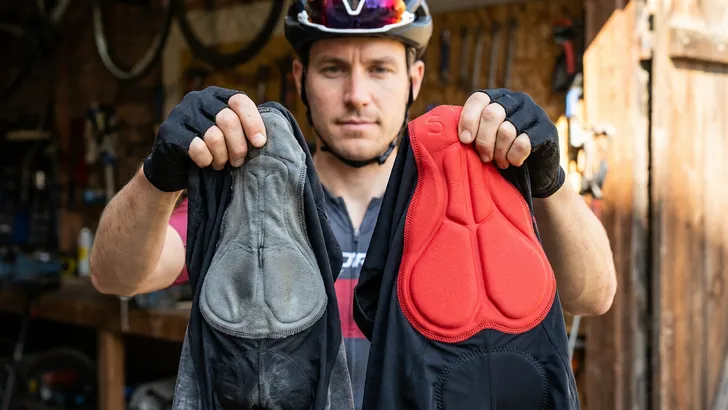 en mannelijke wielrenner vergelijkt de zeem van twee fietsbroeken door erin te knijpen: de oude zeem is plat en dun, terwijl de nieuwe zeem dik en veerkrachtig is.
