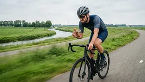 Een wielrenner met helm kijkt met een vies en gefrustreerd gezicht naar een droge energiereep die hij onderweg op de fiets probeert te eten.