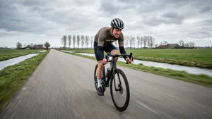 Mannelijke wielrenner met helm rijdt geconcentreerd een solo training op de racefiets op een lege weg.