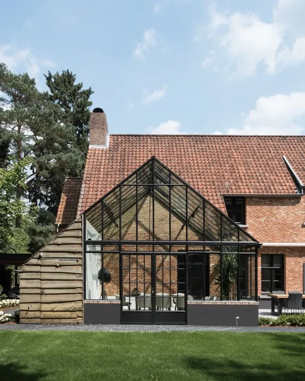 De glazen serre met zwarte stalen kozijnen tegen de bakstenen villa van Mathieu van der Poel en Roxanne Bertels.