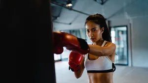 Young Asia lady kickboxing exercise workout punching bag tough female fighter practice boxing in gym fitness class. Sportswoman recreational activity, functional training, healthy lifestyle concept.