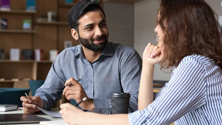 Interview of happy smiling indian hr manager with latin young professional and friendly support discussing job cv. Mentoring Hispanic male teacher and female student in multiethnic creative space.