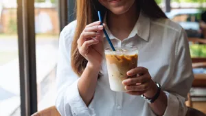 Closeup image of a beautiful young asian woman holding and drinking iced coffee