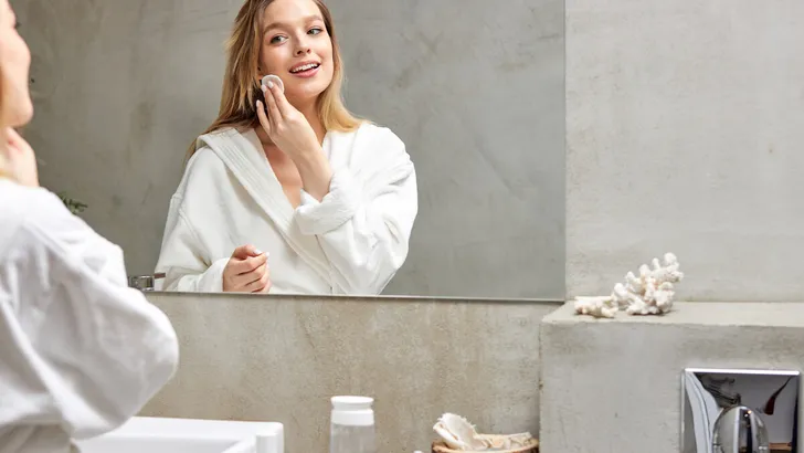 Charming woman in bathrobe applying moisturizing cleansing serum for face and neck in bathroom