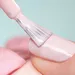 Close-up foto van nagel die wordt gelakt met lichtroze nagellak tegen lichtblauwe achtergrond.