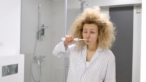 Vrouw staat voor de badkamerspiegel en poetst haar tanden met een flinke kater na oud en nieuw.