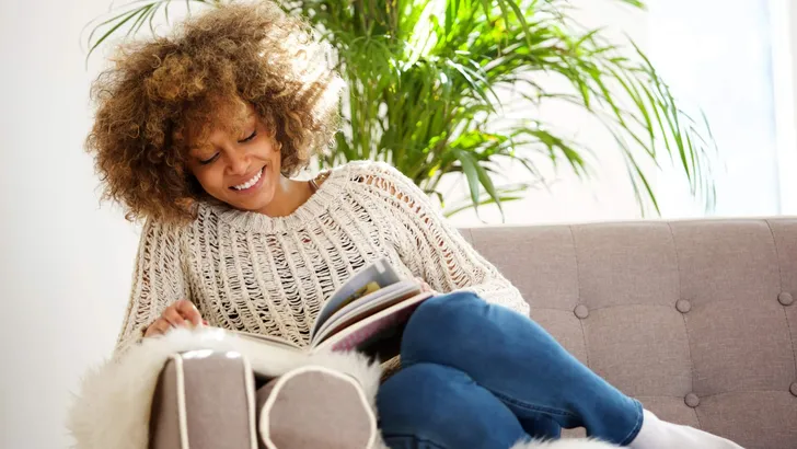 attractive african american woman sitting on sofa reading book