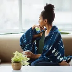 Thoughtful young female wrapped in blanket having coffee on sofa at home